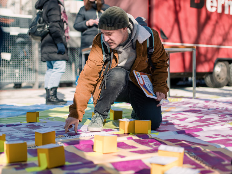 Ein Bürger klebt einen gelben Würfel mit seiner Innenstadtidee auf die Bodenkarte